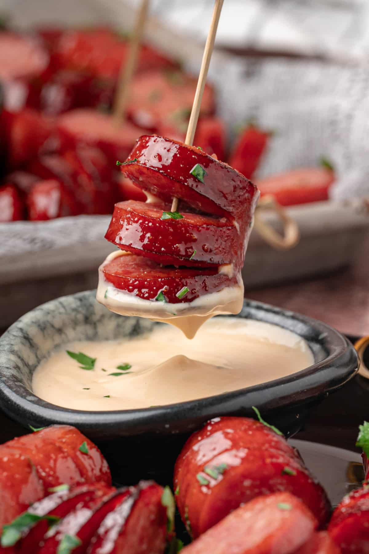 Close-up of a glazed honey garlic kielbasa bite on a skewer with creamy honey mustard.