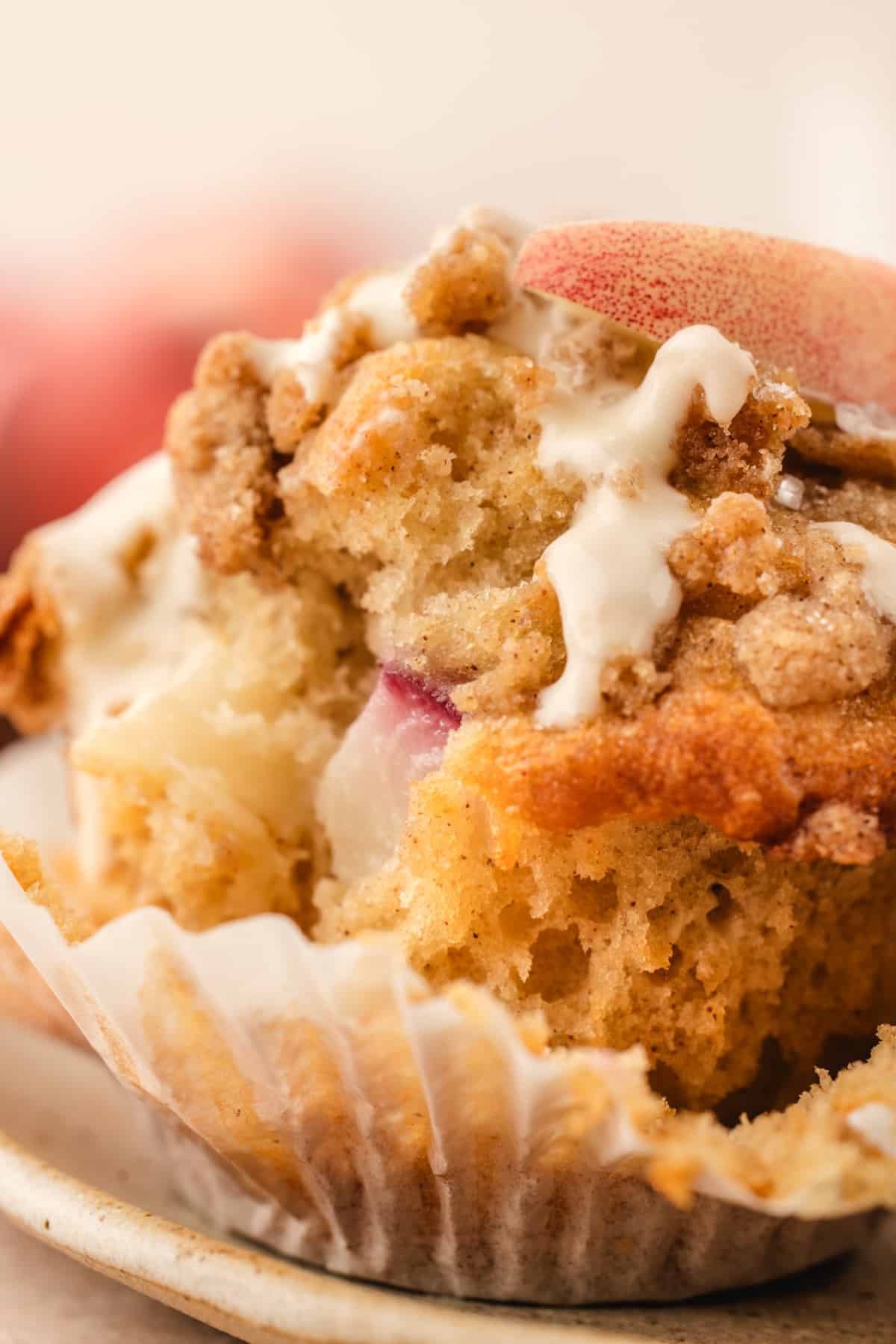 Close-up showing fresh peaches inside a peach coffee cake muffin Close-up of the inside of a peach coffee cake muffin with fresh peach pieces, cinnamon streusel, and vanilla glaze