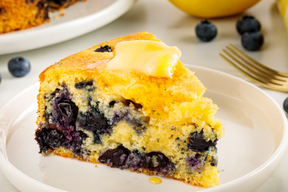 Slice of lemon blueberry cornbread served with butter and honey, showing the tender crumb and fresh blueberries.