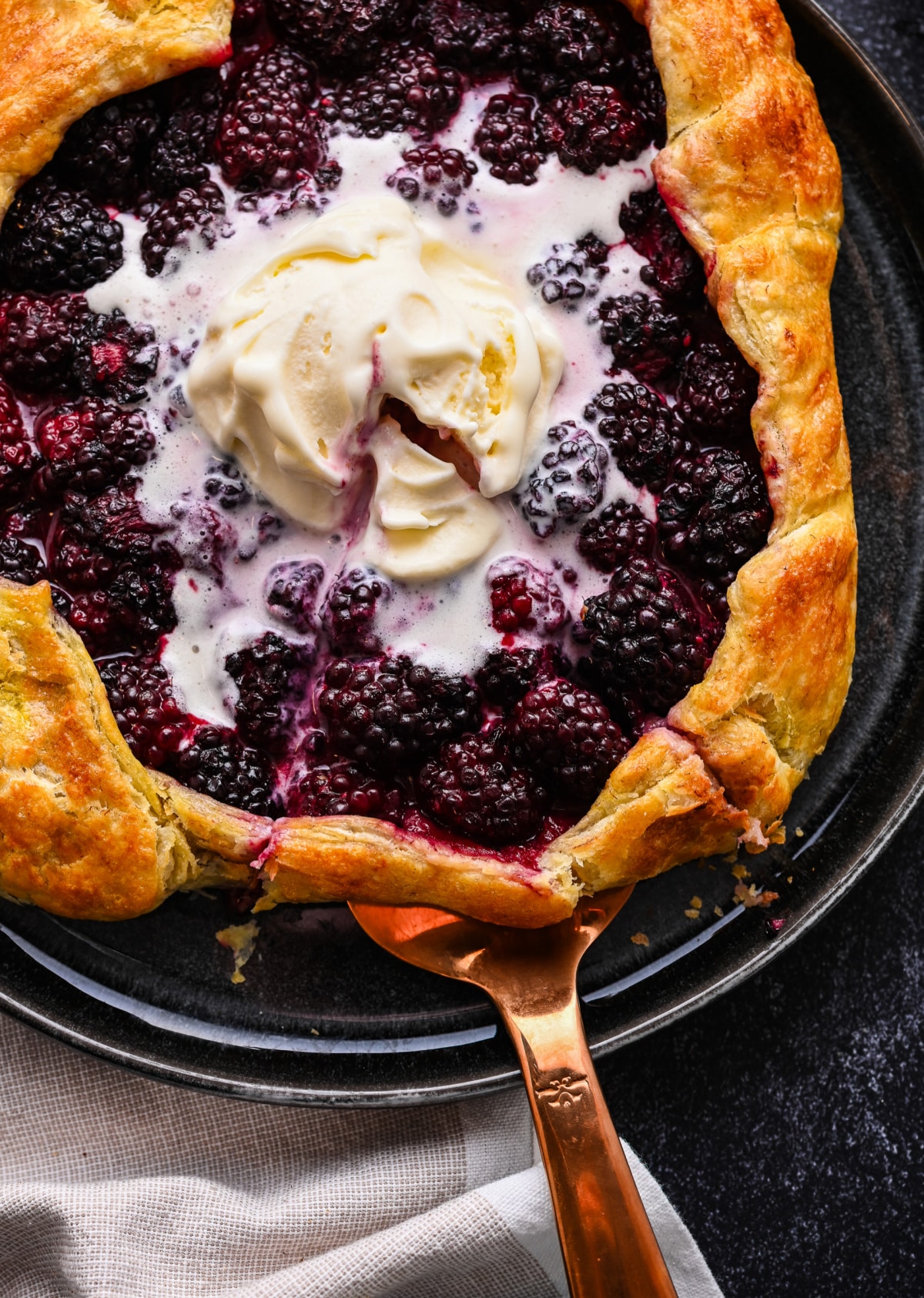 Pie server lifting blackberry puff pastry galette topped with vanilla ice cream.