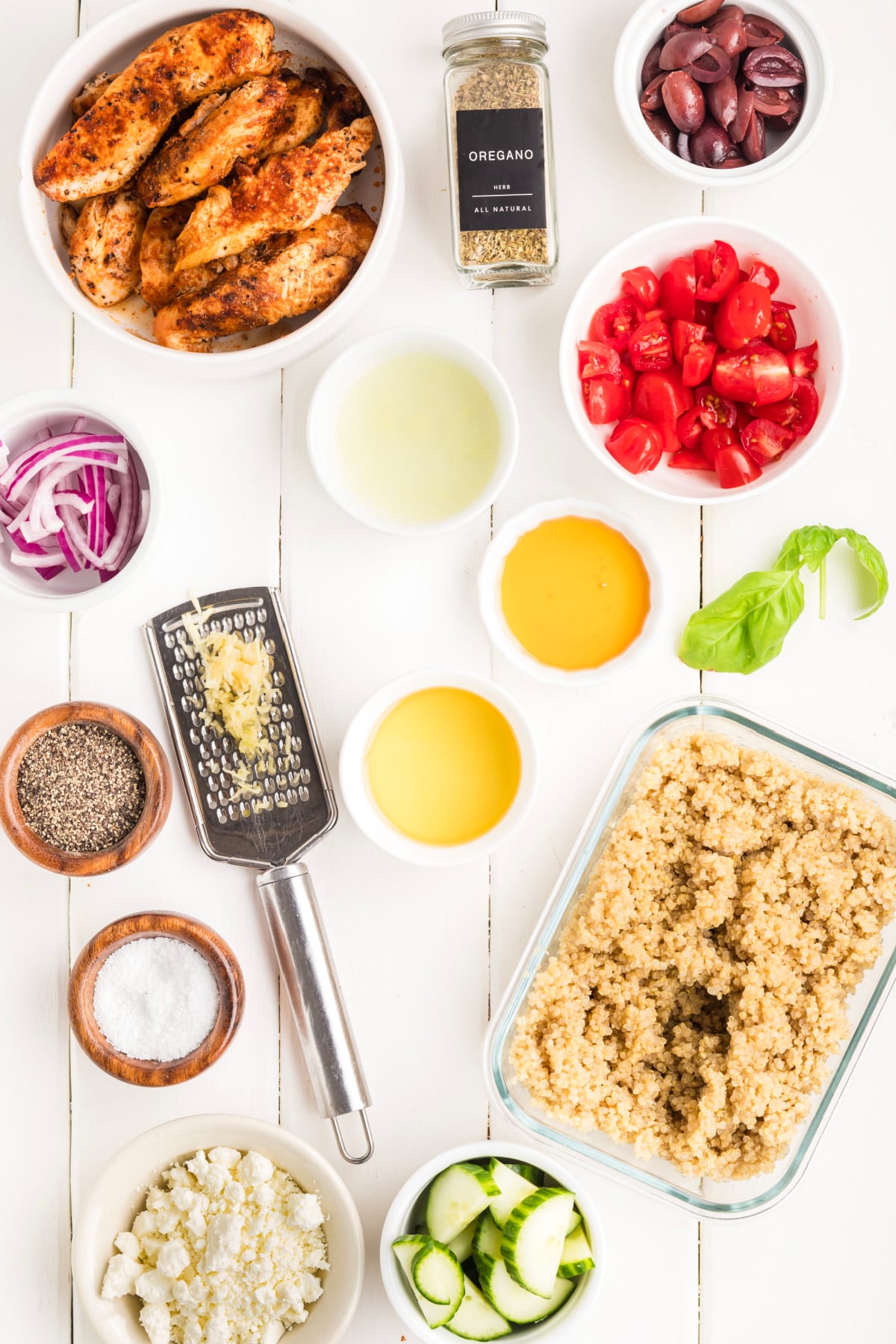 Ingredients for Mediterranean chicken bowl including grilled chicken, cooked quinoa, cucumber, cherry tomatoes, Kalamata olives, feta, red onion, basil, lemon juice, olive oil, garlic, oregano, salt, pepper, and honey.