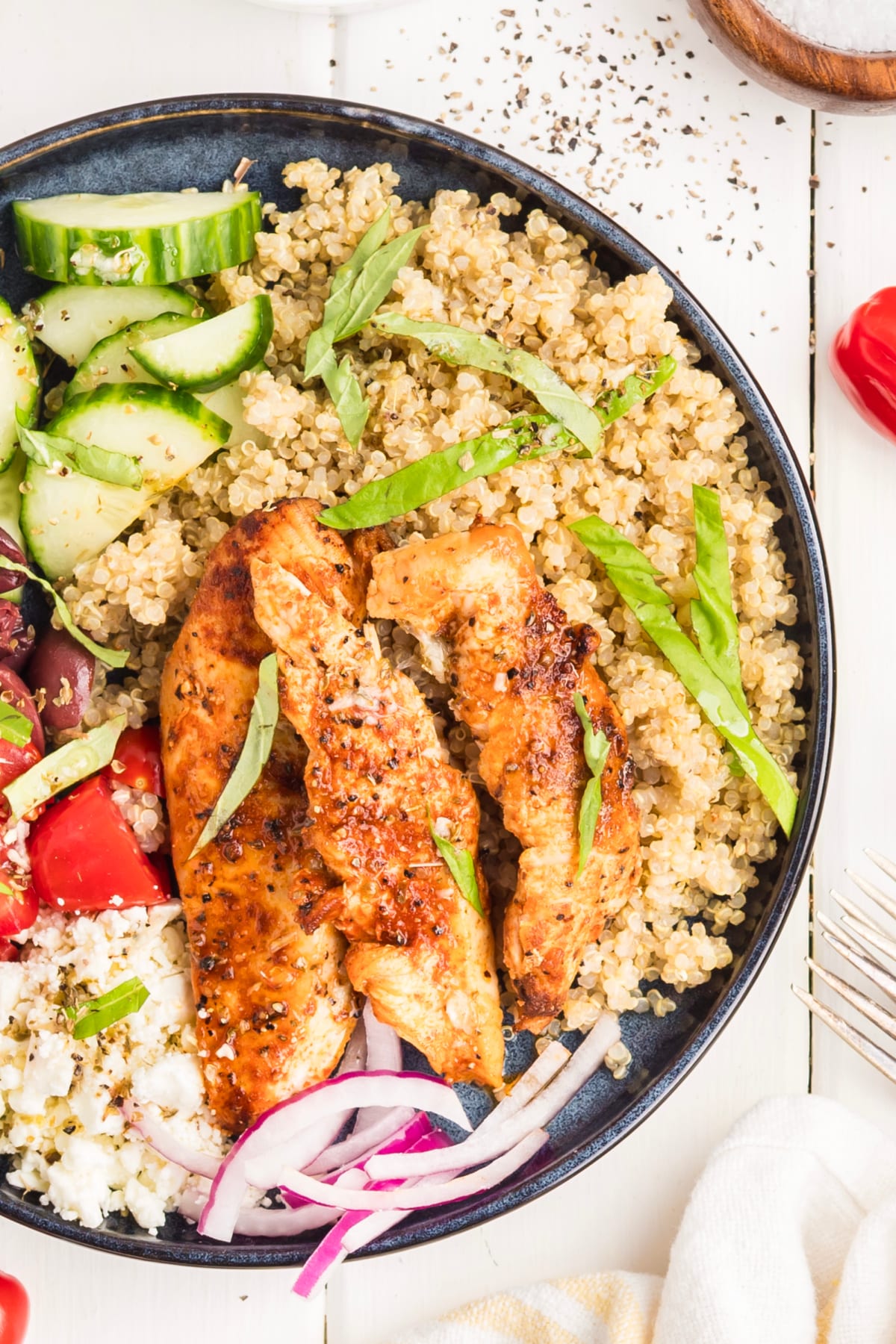 Close-up of grilled chicken served over quinoa with fresh basil in a Mediterranean chicken bowl.