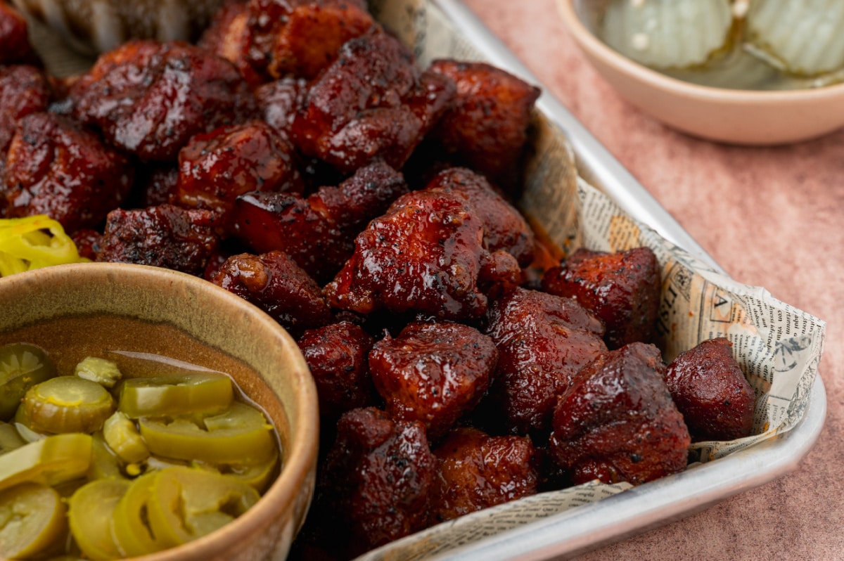 Close-up of Peach Tea Pork Belly Burnt Ends coated in a sticky caramelized peach tea glaze with sliced pickled jalapeños.