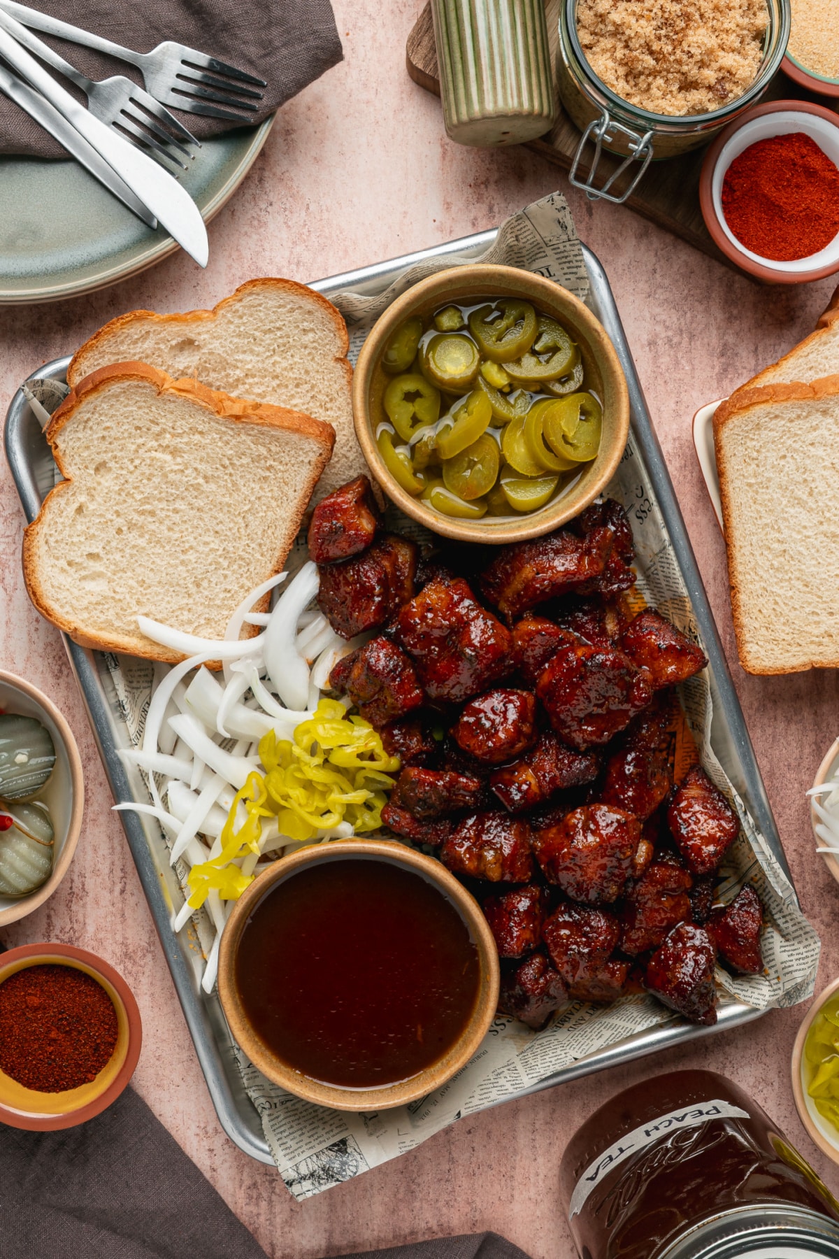 Peach Tea Pork Belly Burnt Ends served on a tray with sliced bread, pickled jalapeños, onions, and extra peach tea glaze.