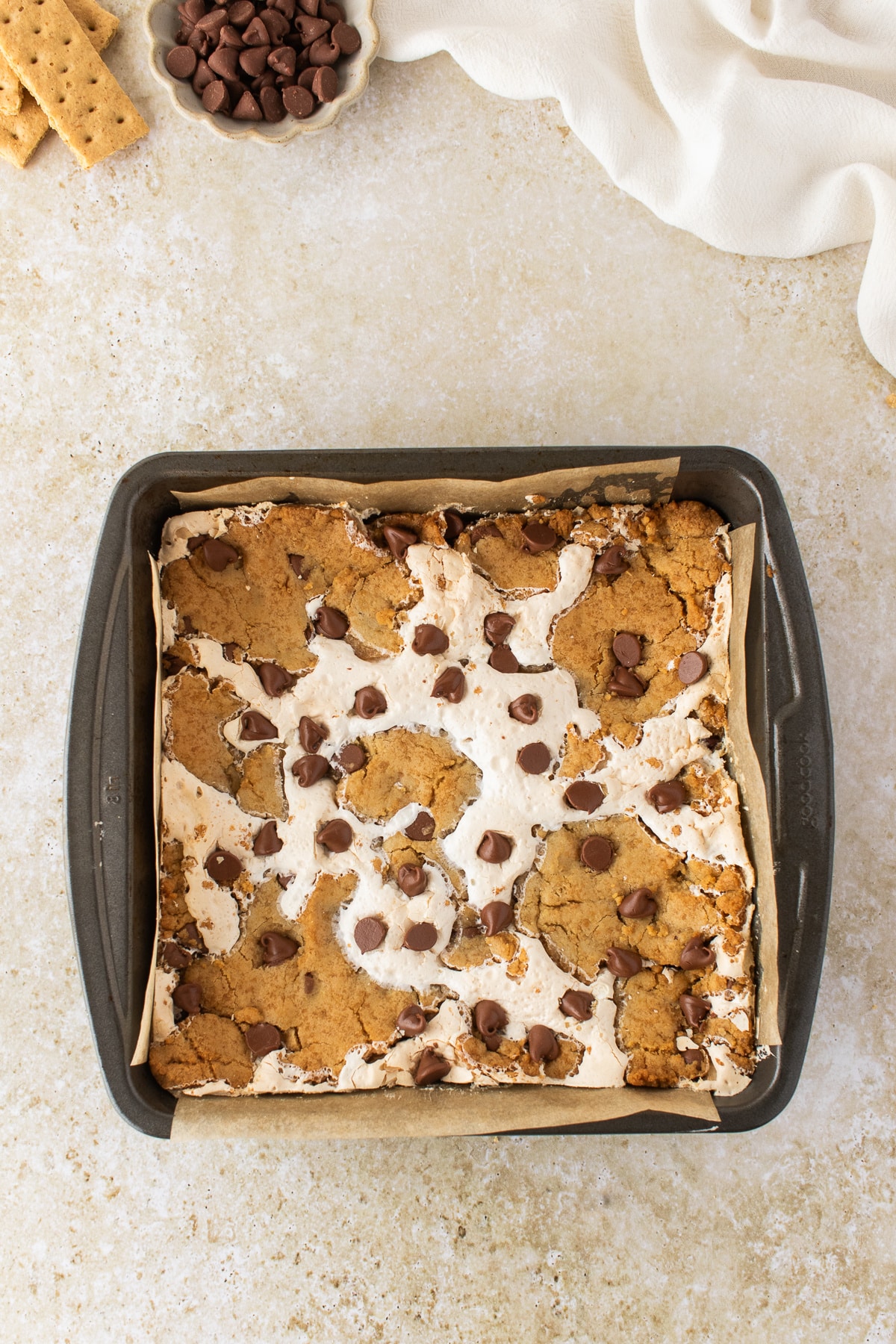 Freshly baked s'mores cookie bars in an 8x8-inch pan with toasted marshmallow and milk chocolate chips.
