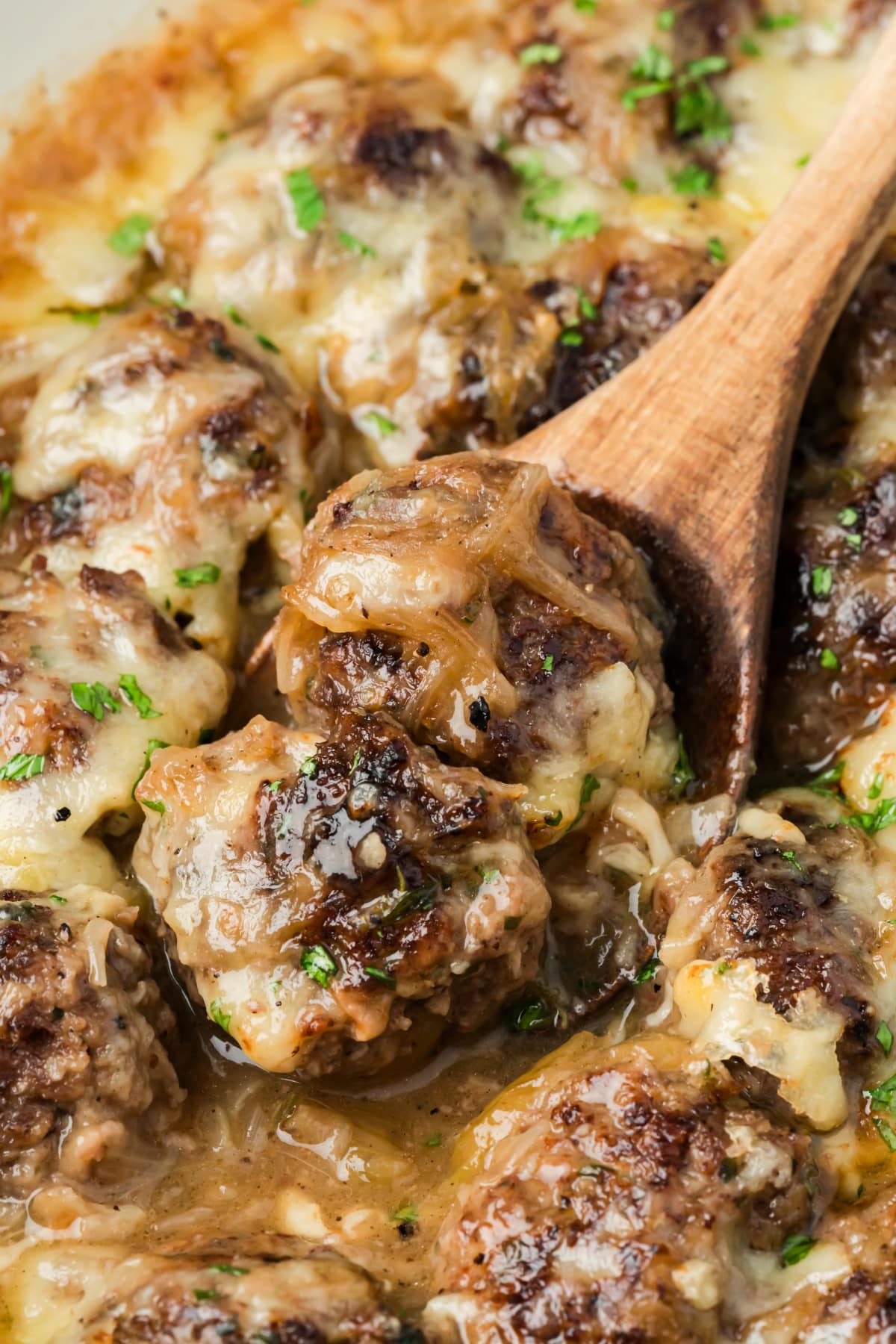 Beef meatballs with caramelized onion sauce and melted Gruyère being served from the skillet