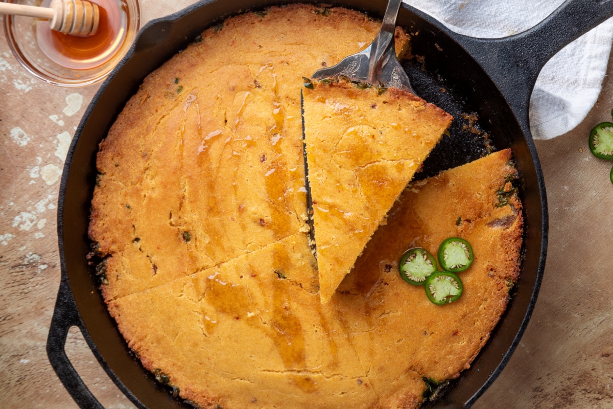 Chipotle hot honey skillet cornbread sliced in a cast-iron skillet with hot honey drizzled over the top