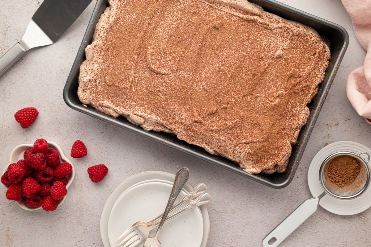 Pan of chocolate cake covered with chocolate whipped cream and a dusting of cocoa powder.