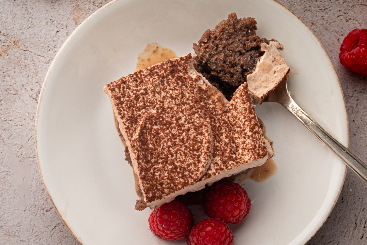 Chocolate tres leches cake with a bite removed, showing the milk-soaked chocolate cake beneath chocolate whipped cream.