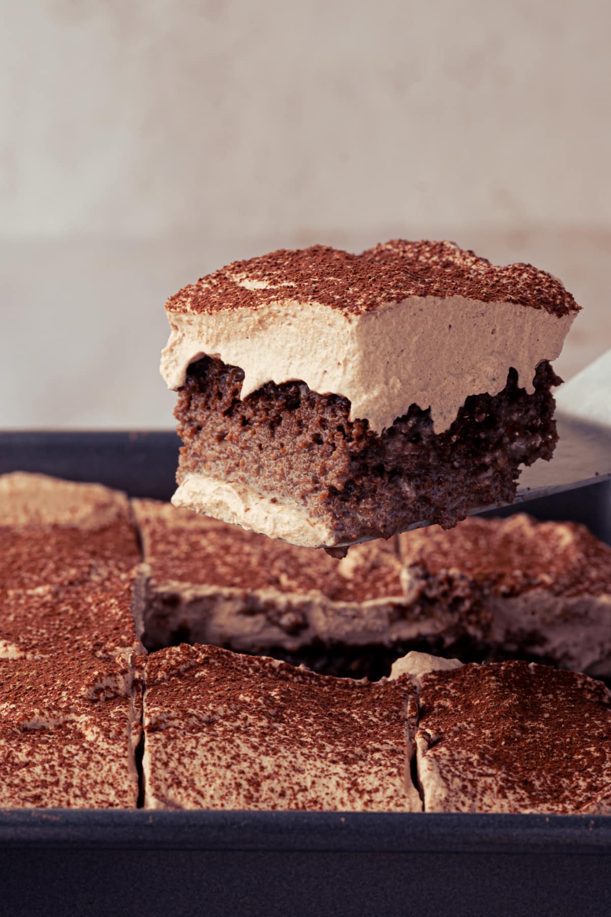 Chocolate cake soaked with three milks and cocoa being lifted from the pan beneath chocolate whipped cream.