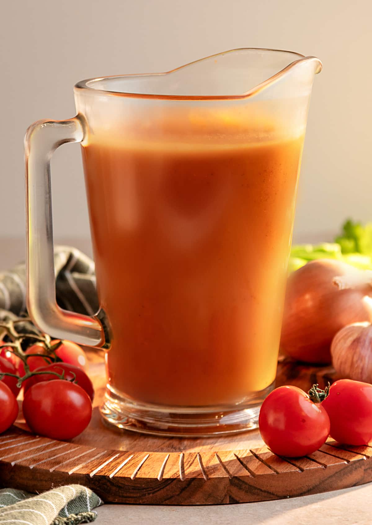 Homemade smoked Bloody Mary mix in a glass pitcher surrounded by fresh tomatoes, onion and garlic
