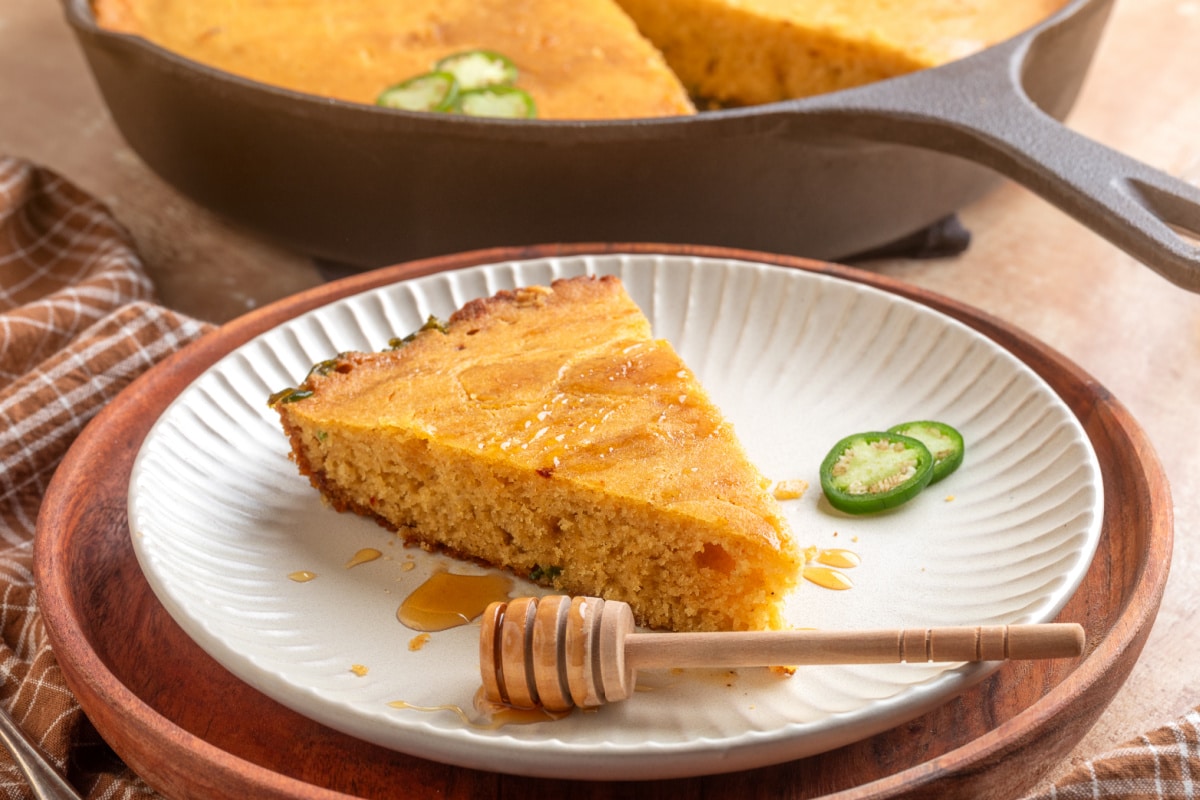 Slice of hot honey jalapeño cornbread served with the cast-iron skillet in the background