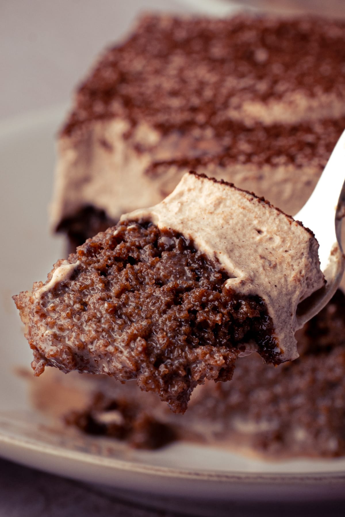 Forkful of milk-soaked chocolate cake with chocolate whipped cream showing the moist interior up close.