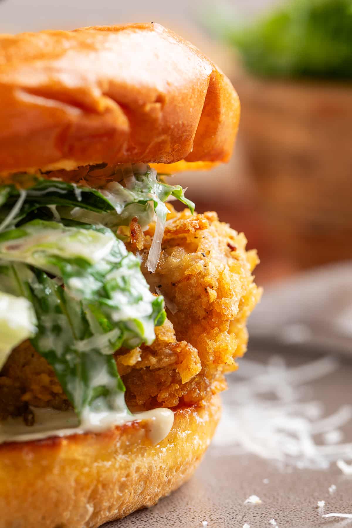 Close-up of a potato chip-crusted chicken Caesar sandwich with homemade Caesar salad, Parmesan cheese, and a toasted brioche bun.
