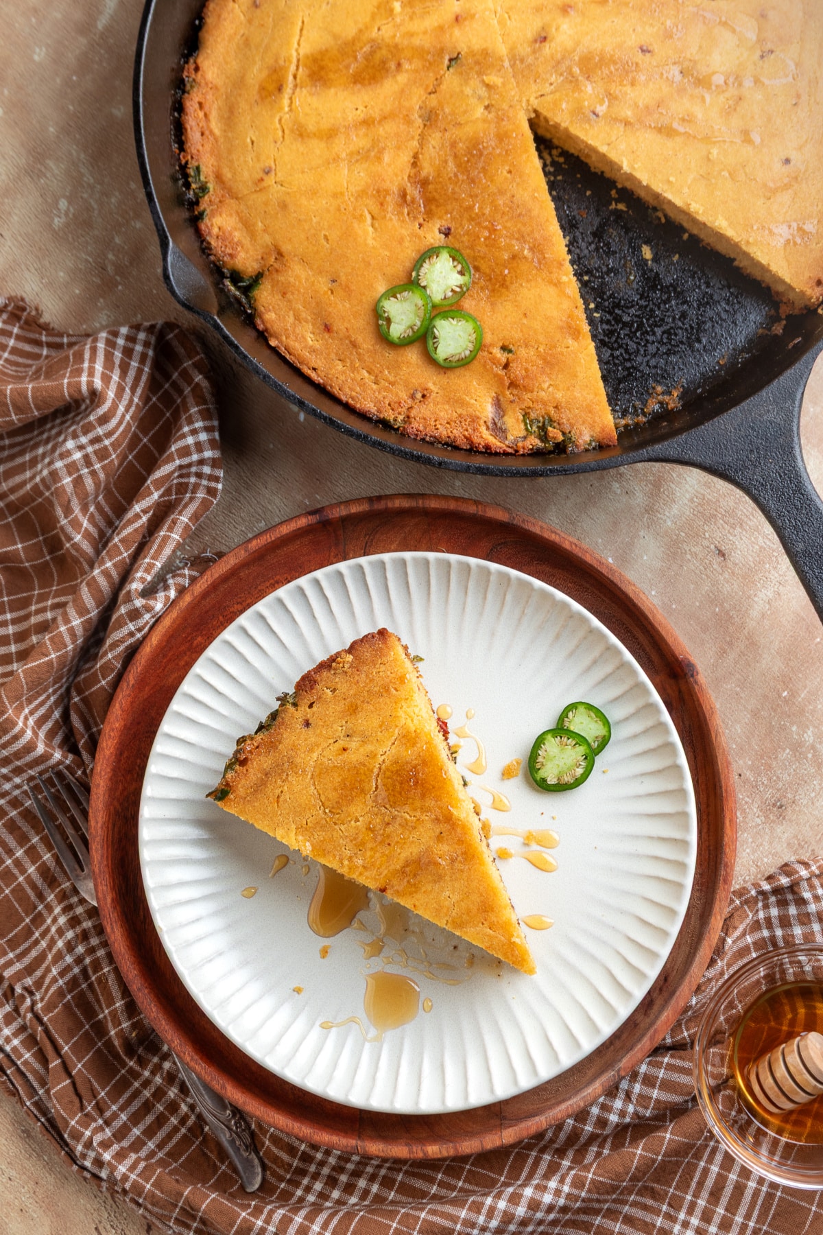 Slice of chipotle jalapeño cornbread served with hot honey beside the cast-iron skillet