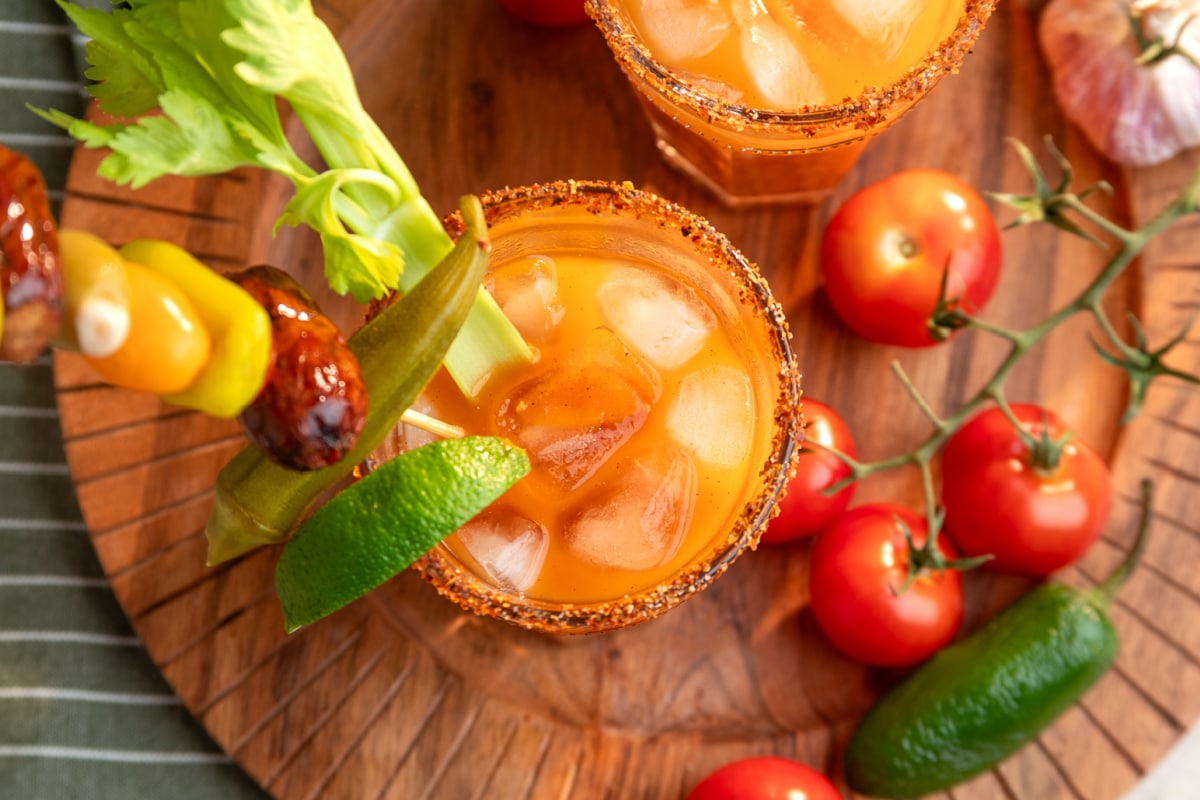 Smoked tomato Bloody Mary cocktail over ice with a Tajín rim, celery, lime, pickled okra and smoked sausage