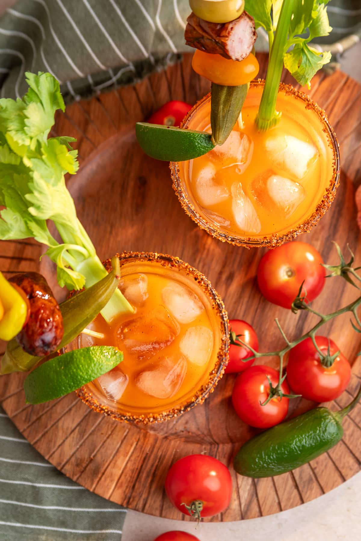 Two smoked Bloody Mary cocktails with Tajín rims, celery, lime, pickled okra, smoked sausage and tomato garnishes