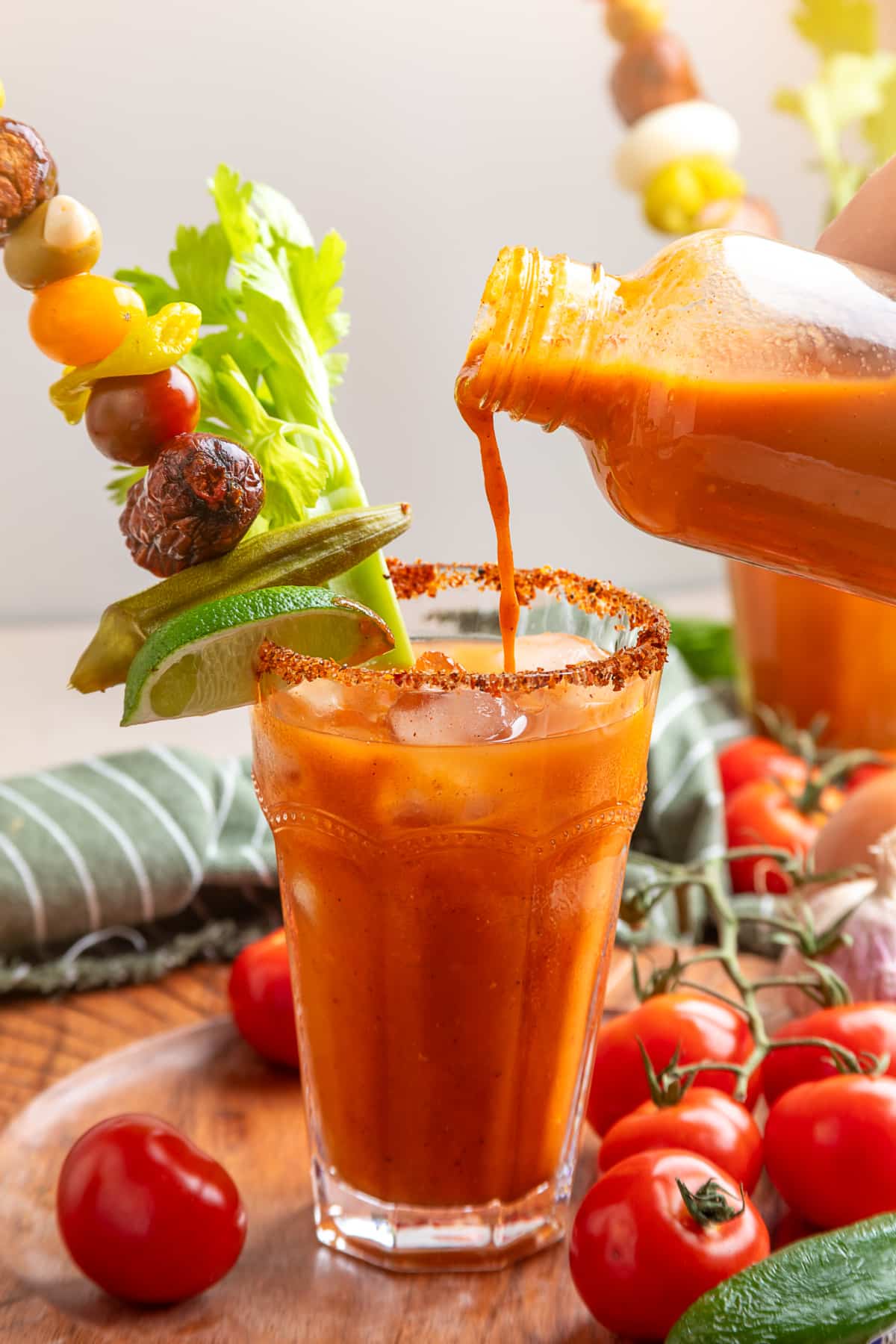 Smoked tomato Bloody Mary mix being poured into an ice-filled glass with a Tajín rim and garnishes