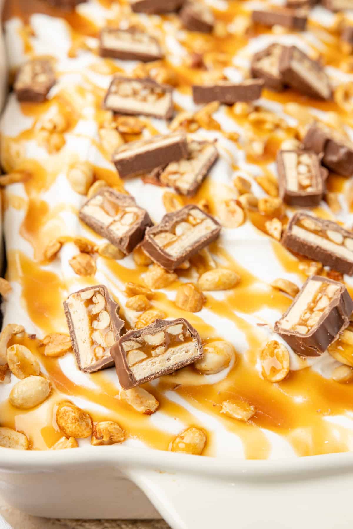 Chopped Snickers bars, caramel and roasted salted peanuts over whipped topping on chocolate cake