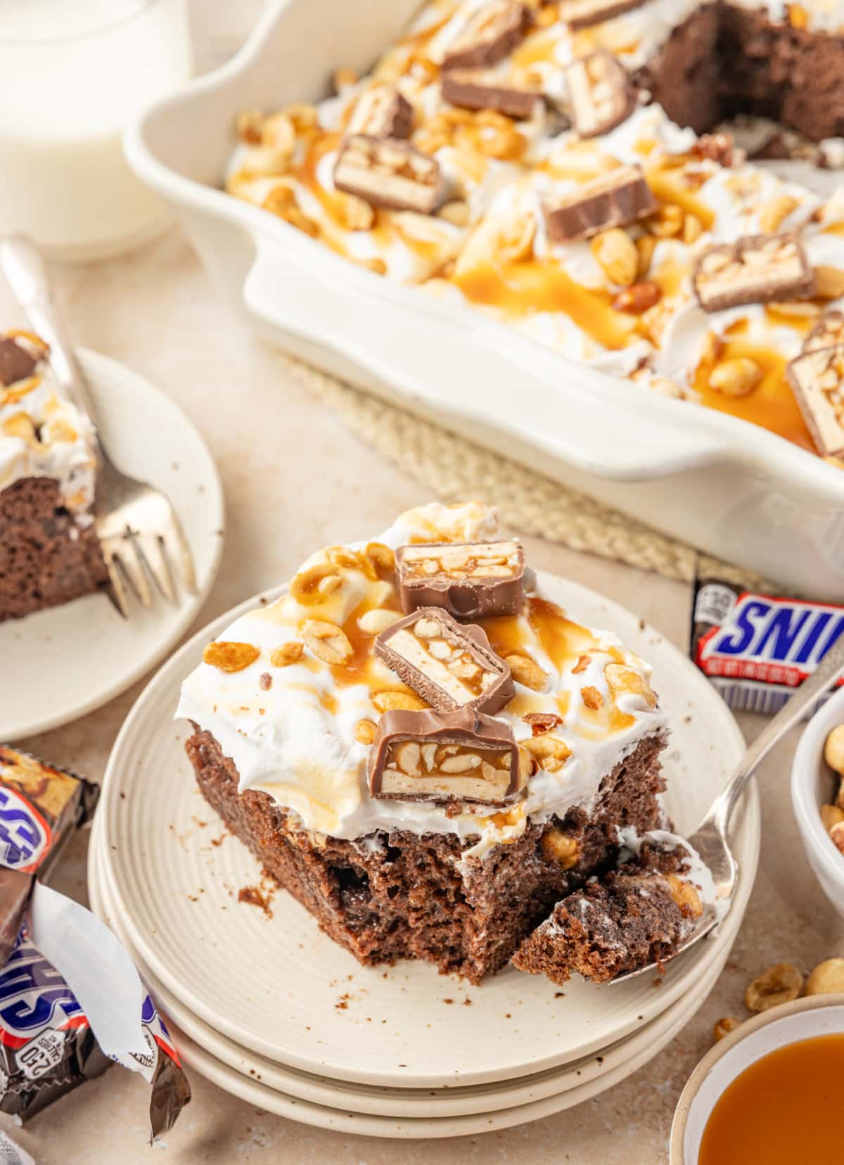 Snickers poke cake slice with chocolate pudding, caramel, salted peanuts and chopped candy bars