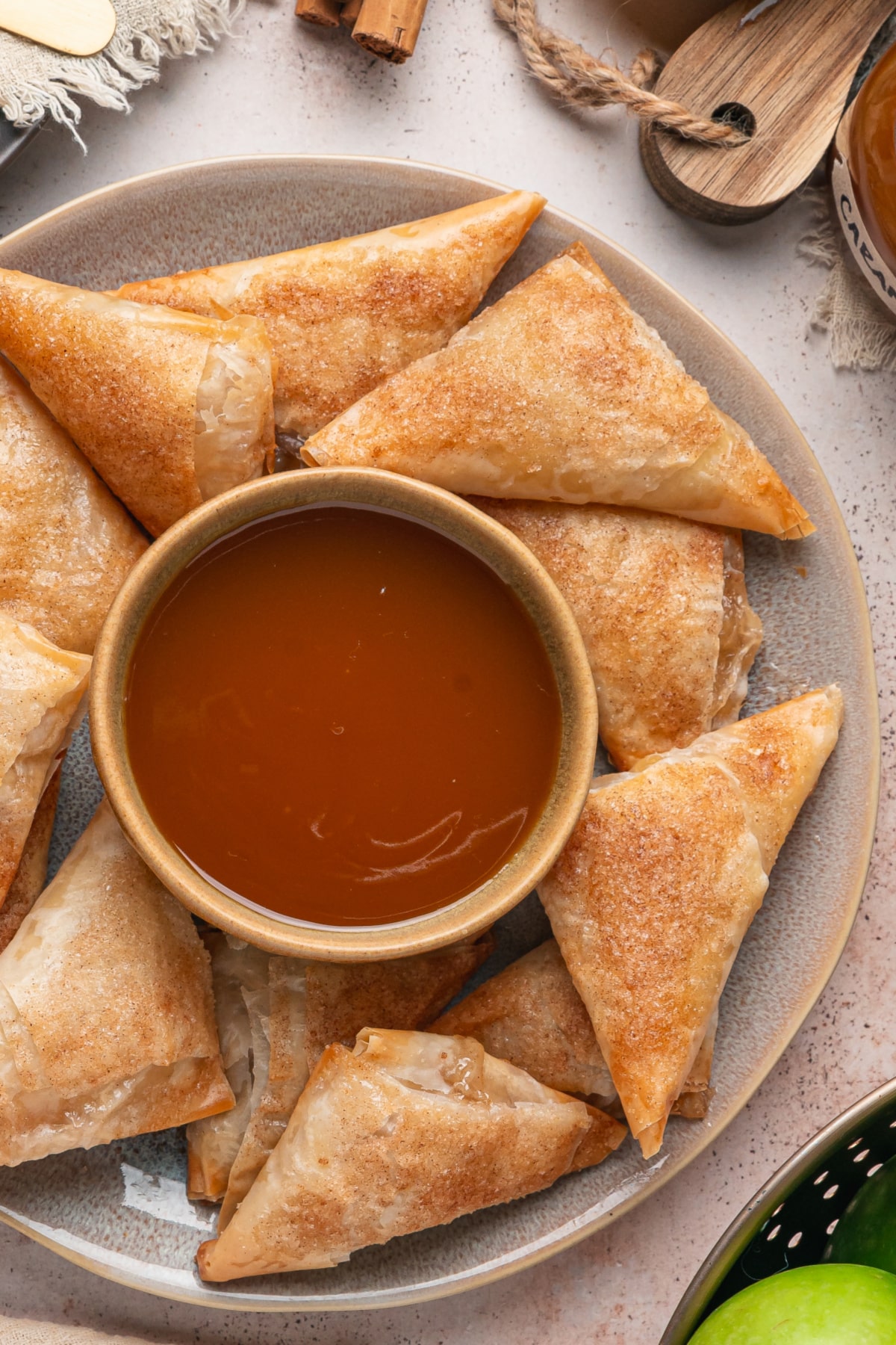 Apple pie samosas made with phyllo dough and cinnamon sugar arranged around a bowl of caramel sauce.
