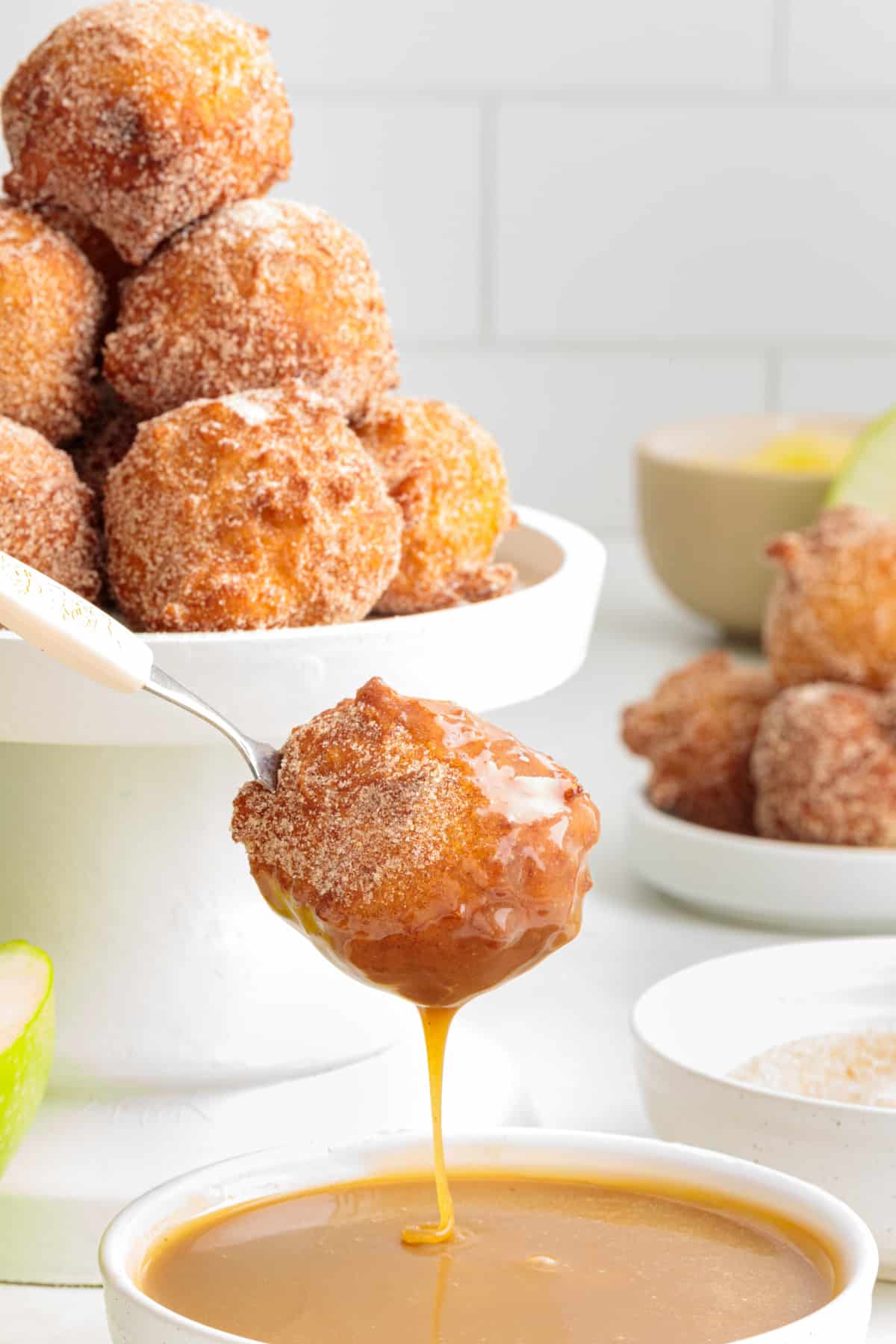 Cinnamon sugar applesauce fritter dipped in maple caramel with more fritters in the background