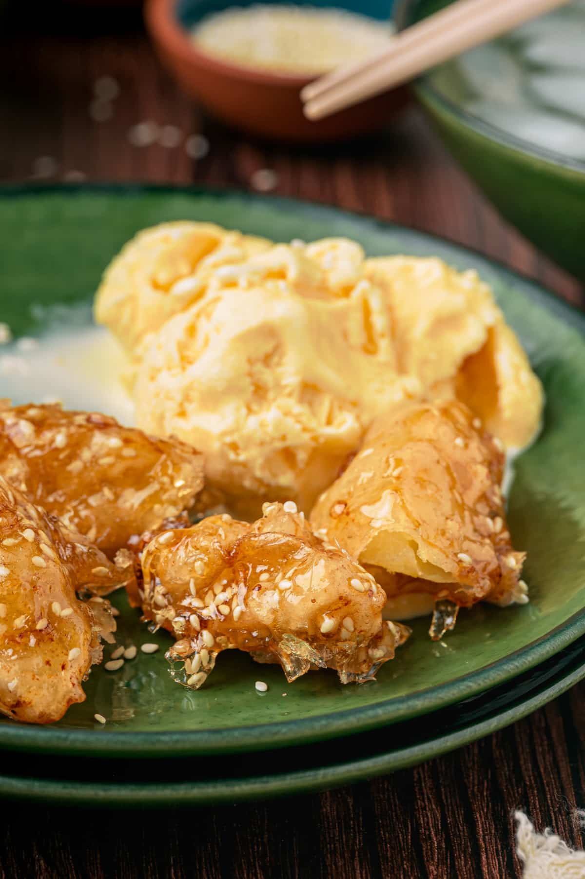 Close-up of fried apple pieces with a thin brittle sesame caramel shell served with vanilla ice cream
