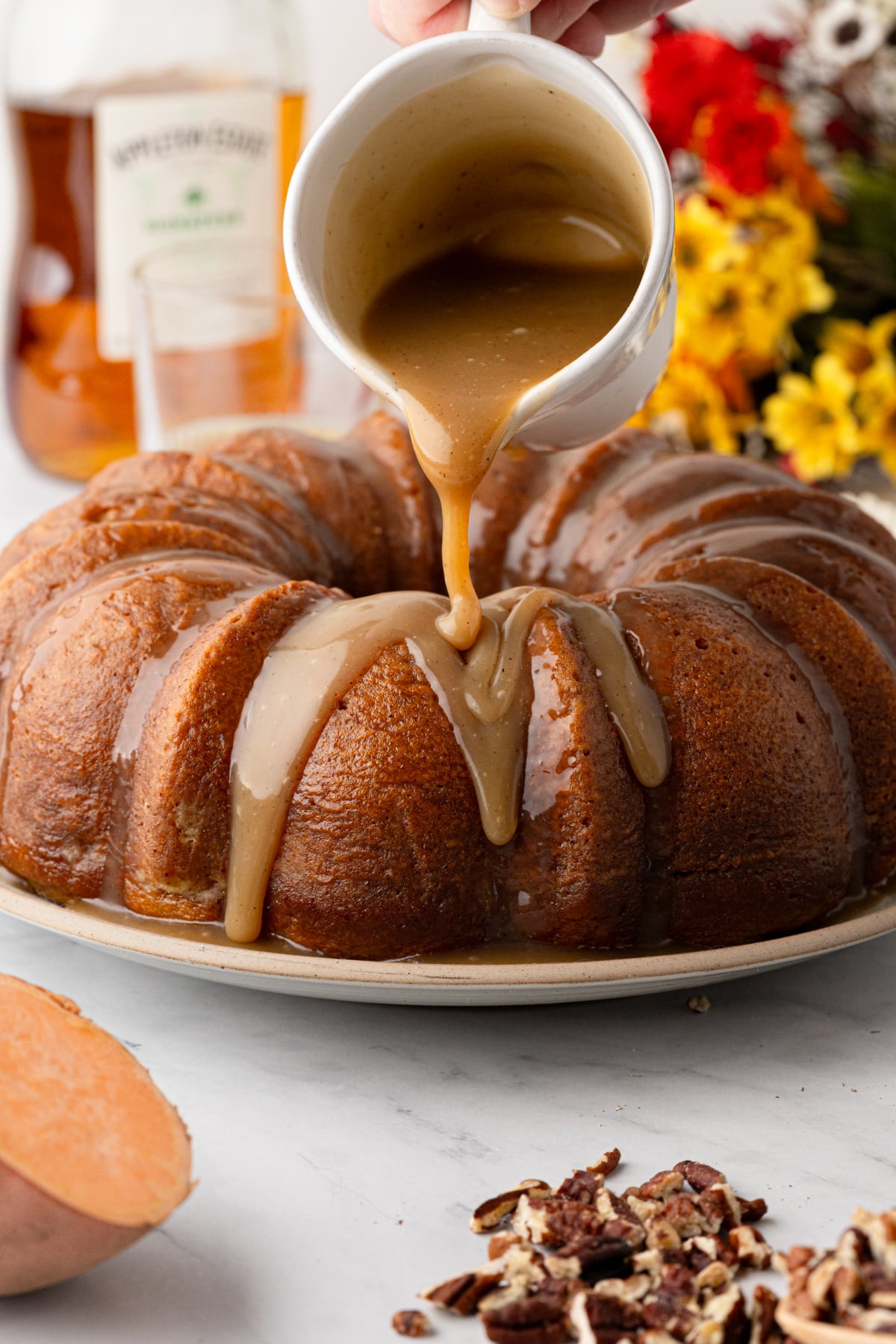 Buttered rum caramel being poured over sweet potato Bundt cake before adding the toasted pecans.