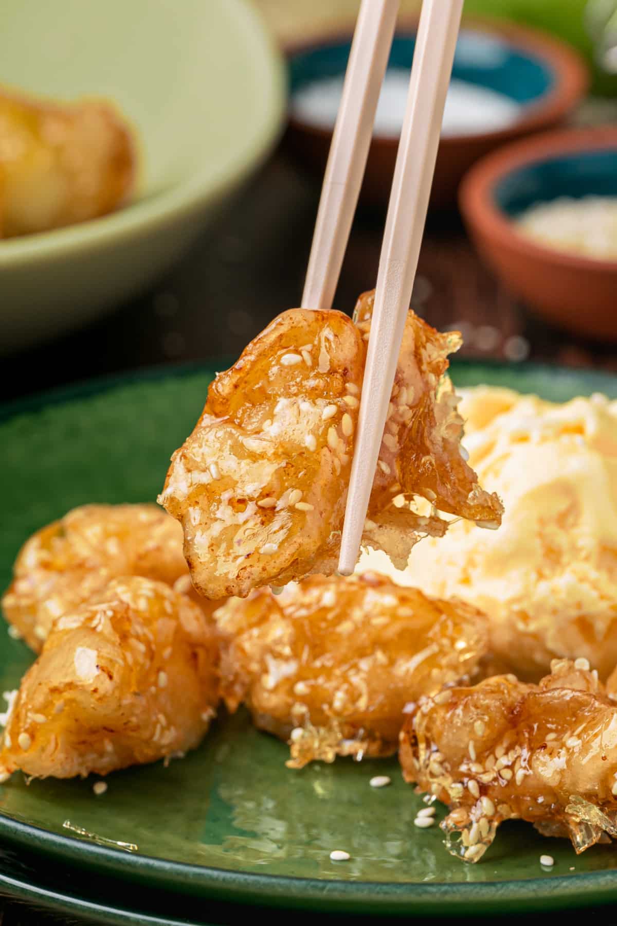Chinese toffee apples with sesame caramel held with chopsticks over a serving plate