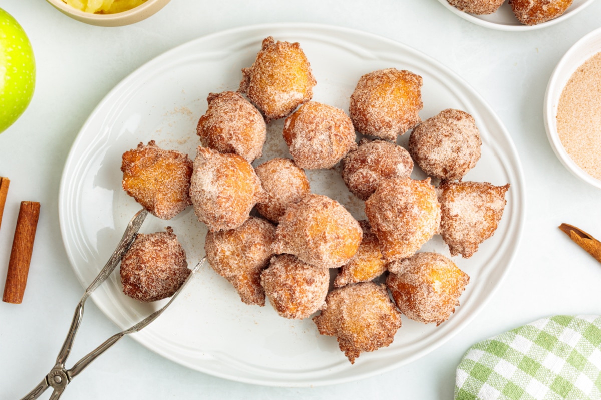 Cinnamon sugar applesauce fritters piled on a white serving platter