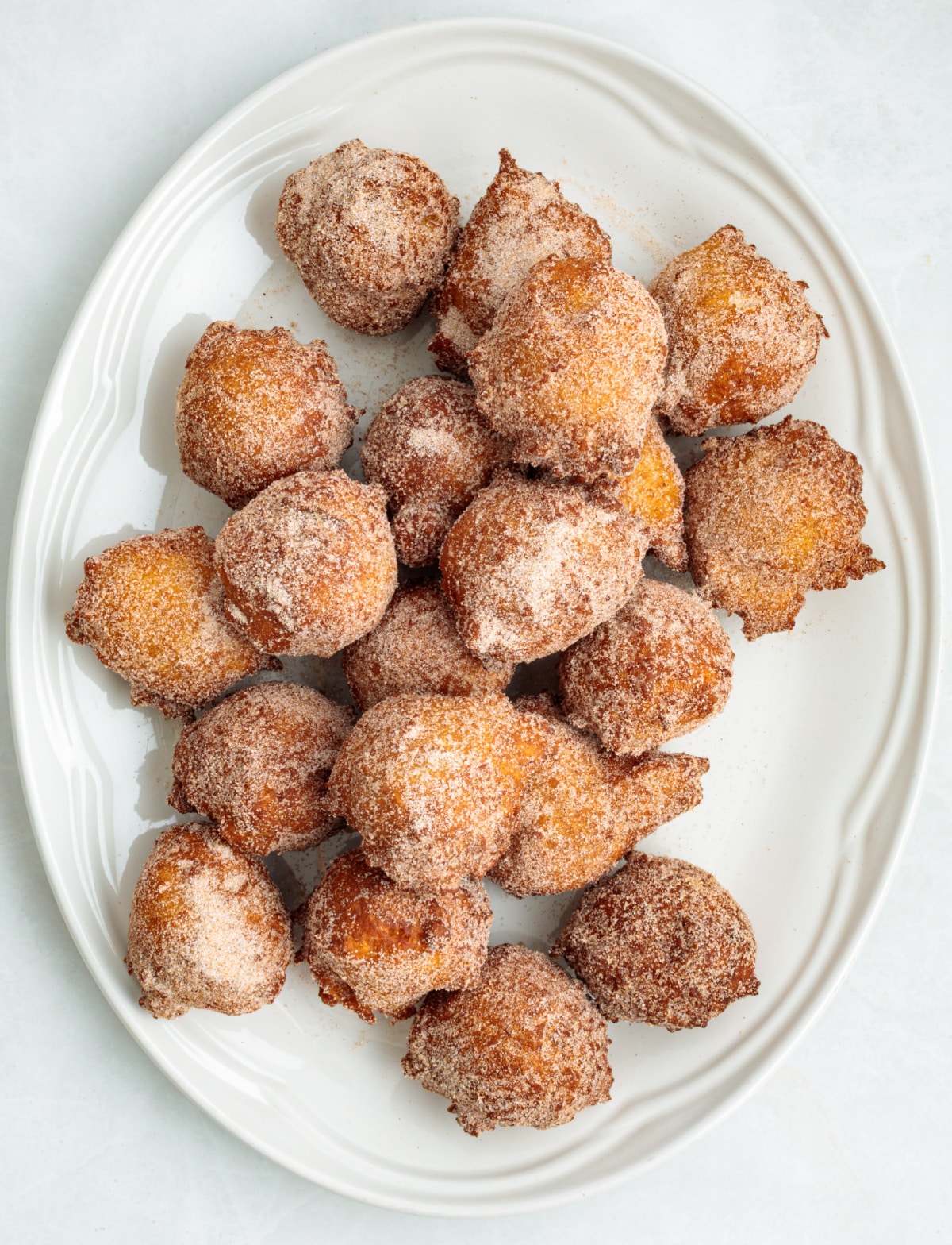 Fried applesauce fritters coated in cinnamon sugar on a white platter