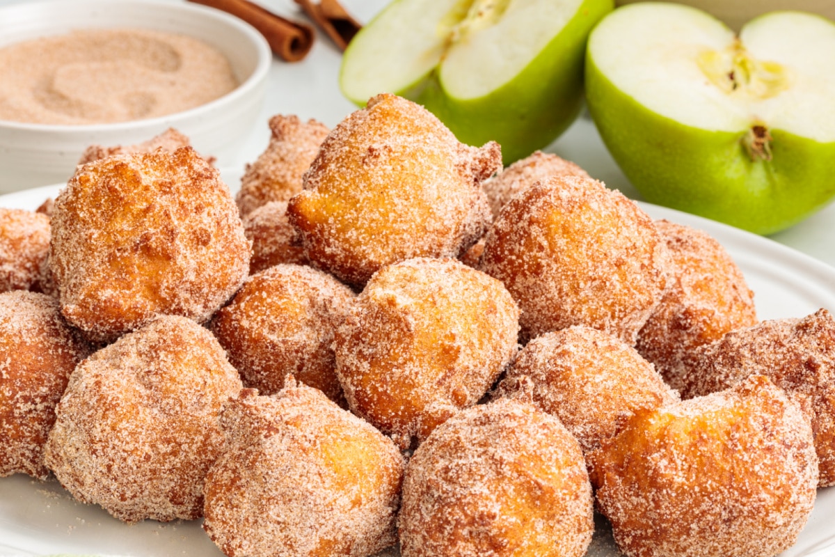 Homemade applesauce fritters coated in cinnamon sugar beside sliced Granny Smith apples