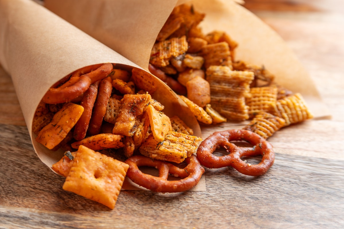 Herbed Chex mix with crackers, pretzels and nuts portioned into paper cones for serving. Baked Chex mix with Cheez-It crackers, Triscuits, pretzels and nuts served in brown paper cones