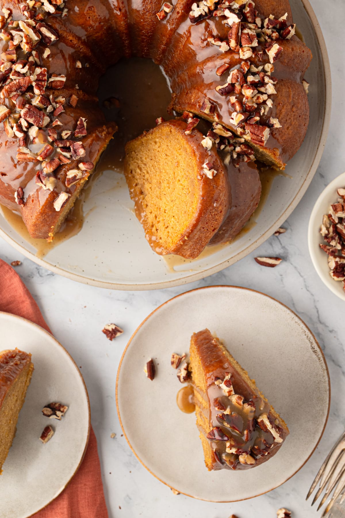Sweet potato Bundt cake with a slice removed and served on a plate, topped with buttered rum caramel and toasted pecans.