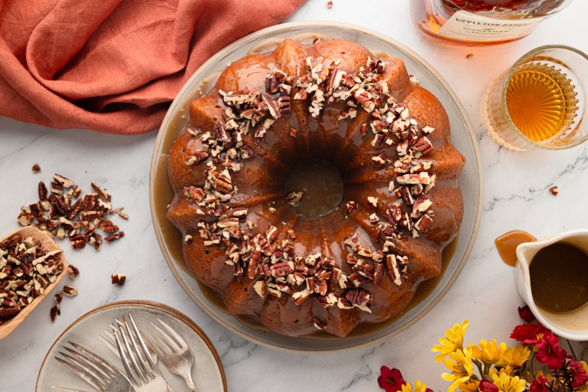 Overhead view of sweet potato Bundt cake with buttered rum caramel, toasted pecans and dark rum alongside.