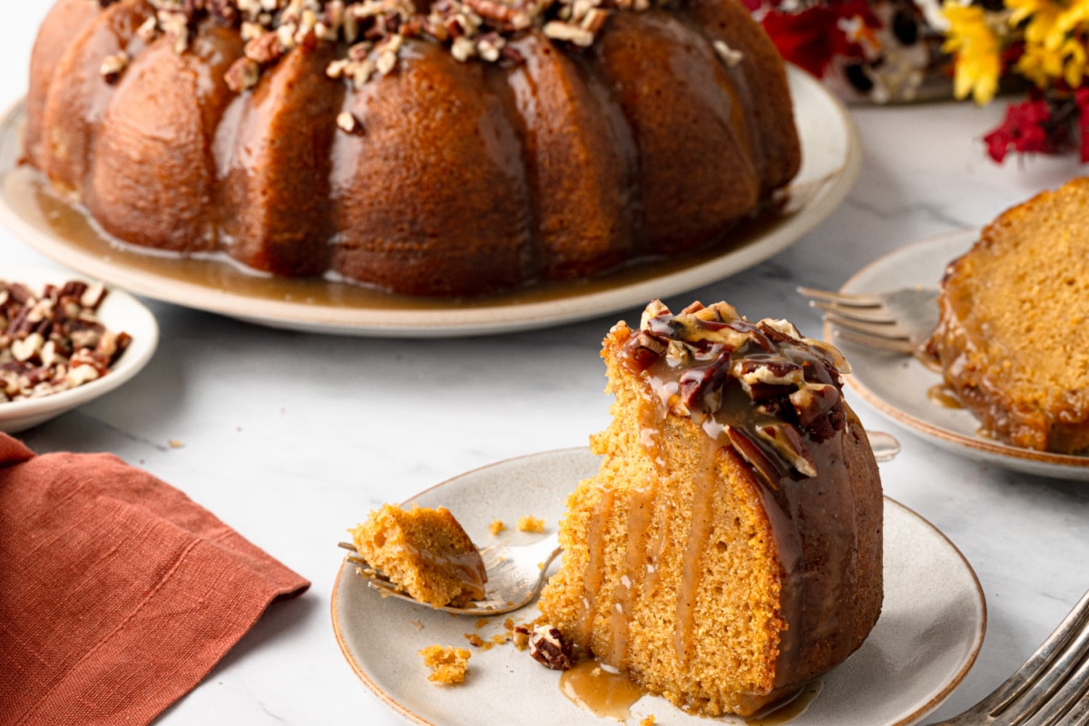 Slice of sweet potato Bundt cake on a plate with buttered rum caramel dripping down the cut side and toasted pecans on top.