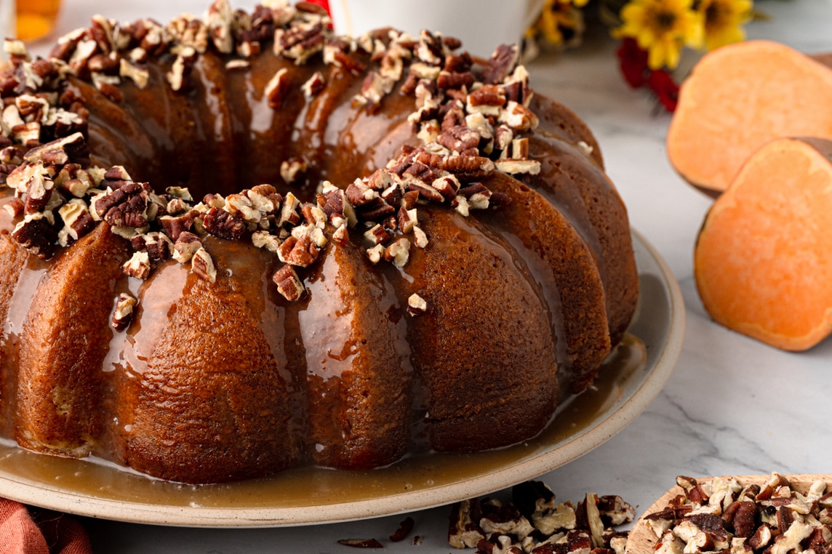 Sweet potato Bundt cake covered with buttered rum caramel and toasted pecans with cut sweet potatoes alongside.