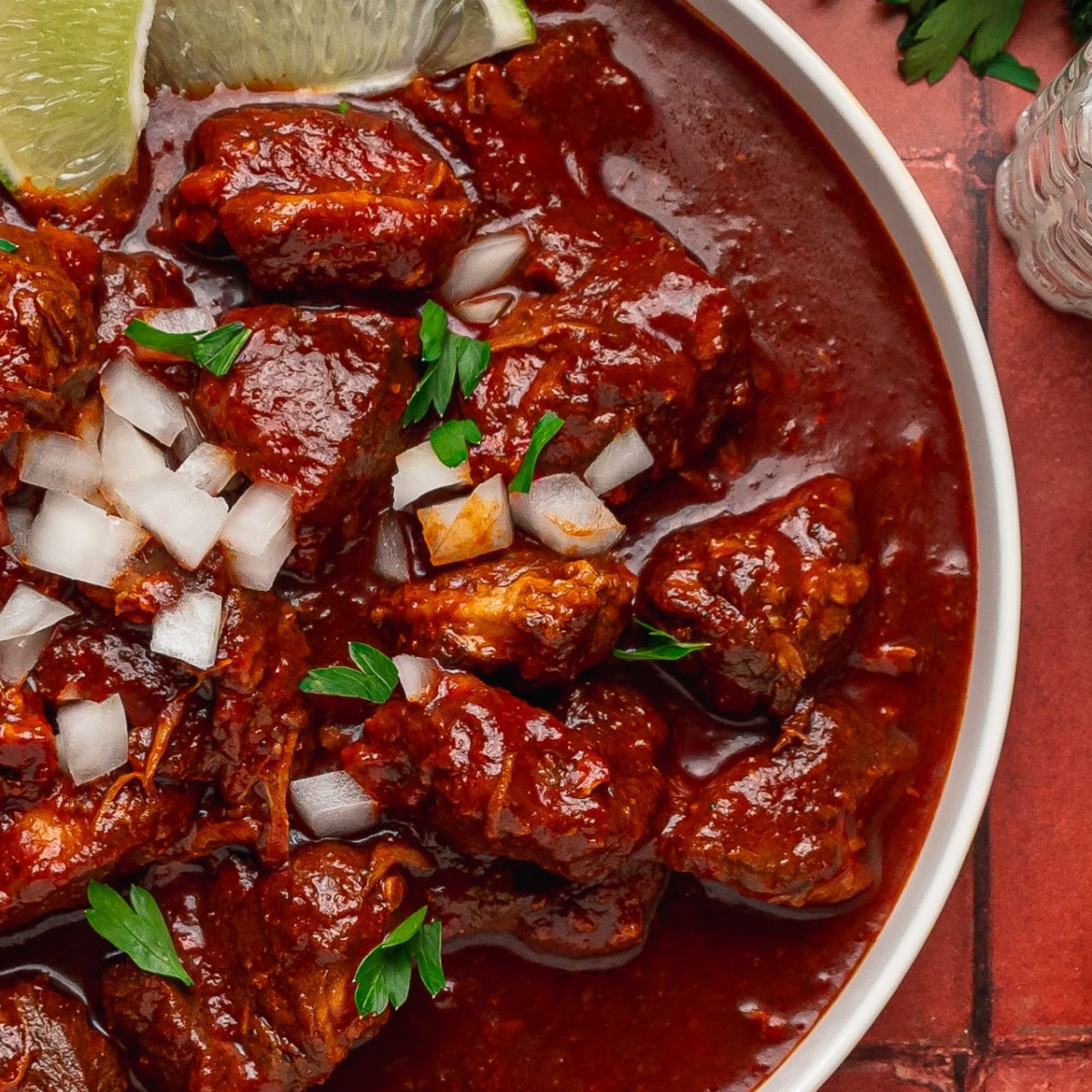 Carne adovada with tender pork shoulder in a red chile sauce topped with chopped onion and parsley