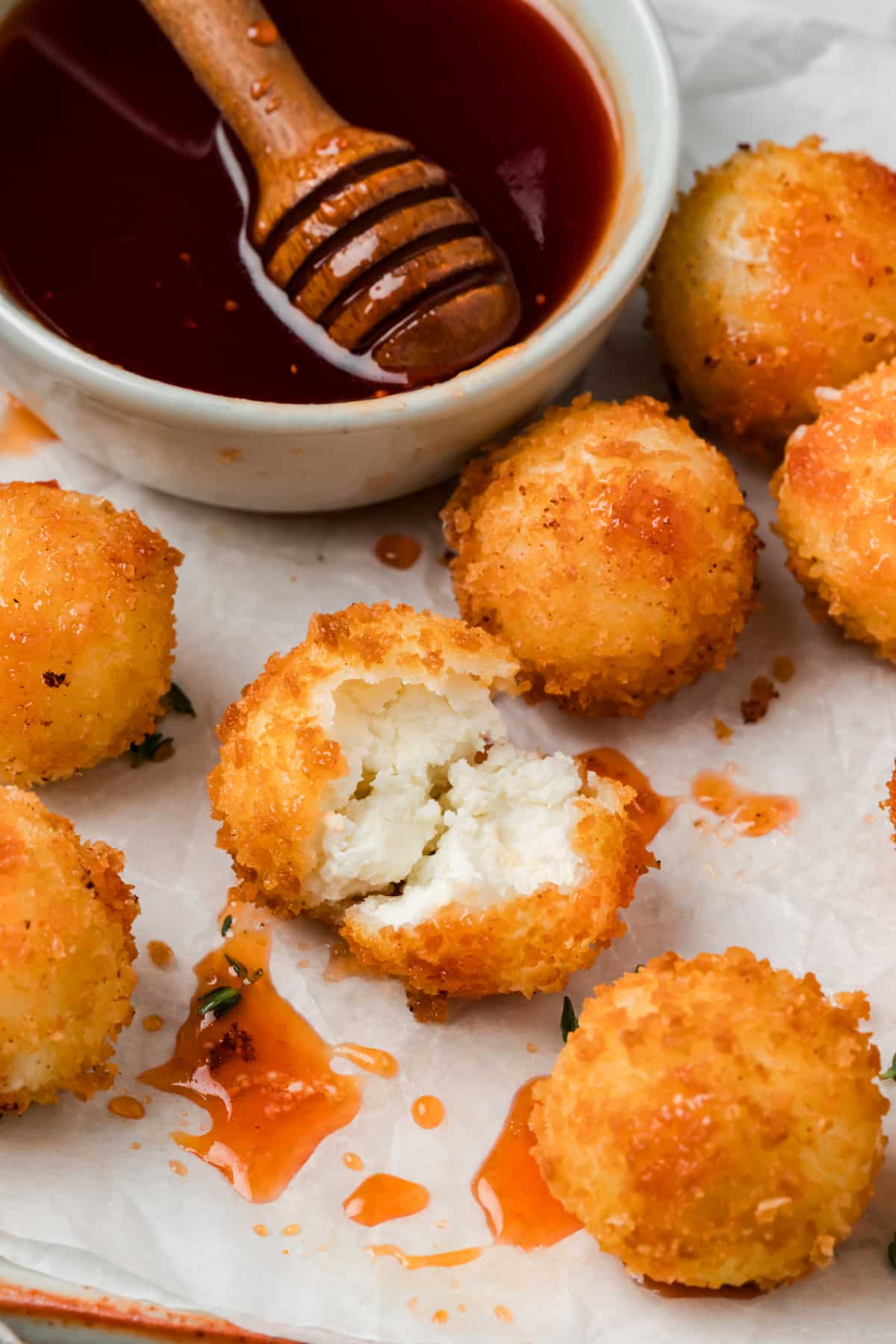 Fried panko-coated goat cheese ball broken open to show its creamy white center, surrounded by cranberry hot honey and more golden cheese balls.