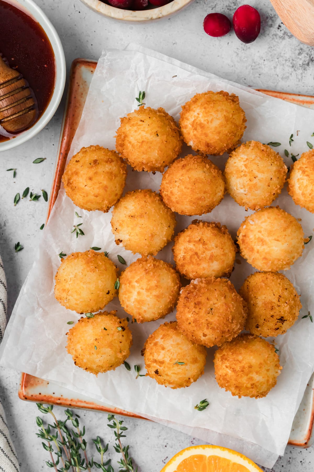 Overhead view of golden panko-crusted goat cheese balls on a parchment-lined platter with cranberry hot honey and fresh thyme.