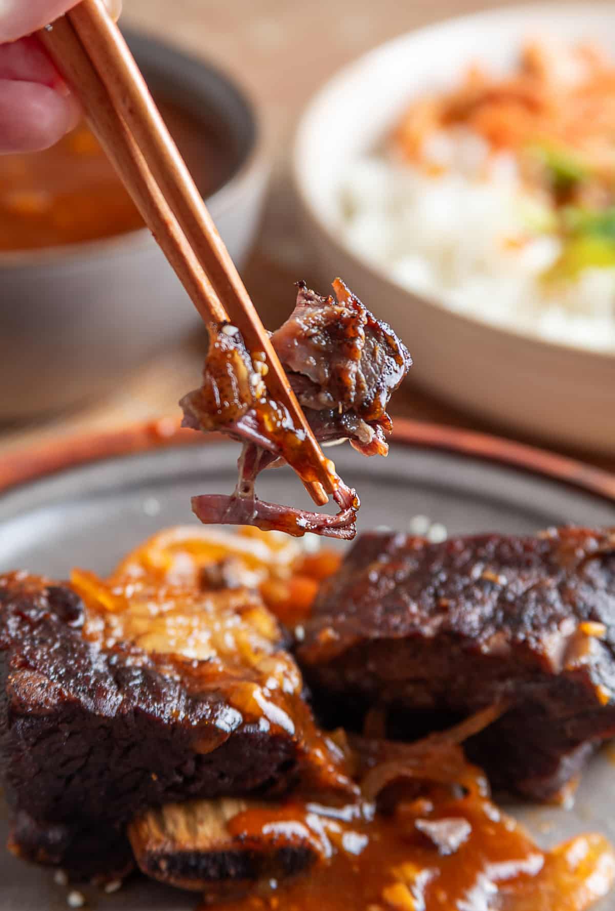 Fork-Tender Slow Cooker Short Ribs with Gochujang Sauce Chopsticks lifting a tender piece of slow-cooked beef short rib coated in gochujang sauce above the remaining ribs.