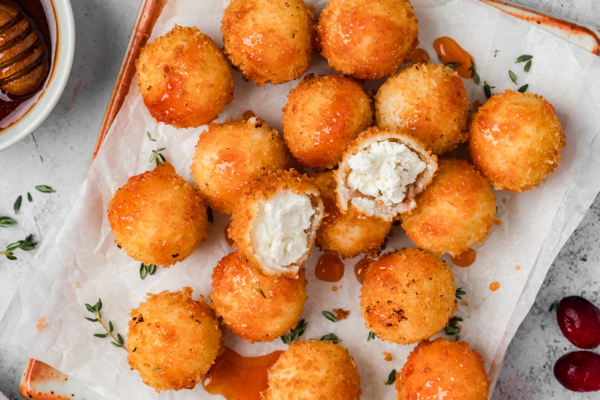 Overhead view of fried goat cheese balls drizzled with cranberry hot honey, with two cut open to reveal their creamy centers.