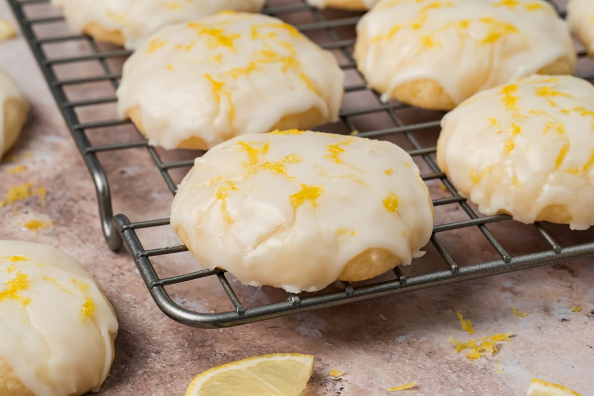 Glazed lemon ricotta cookies topped with fresh lemon zest on a cooling rack