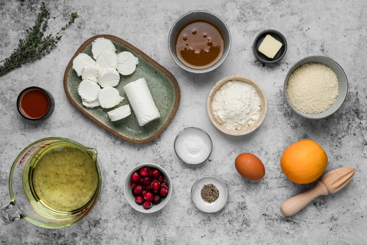 Ingredients for fried goat cheese balls with cranberry hot honey, including goat cheese, panko, flour, cranberries, honey, orange, hot sauce, and thyme.