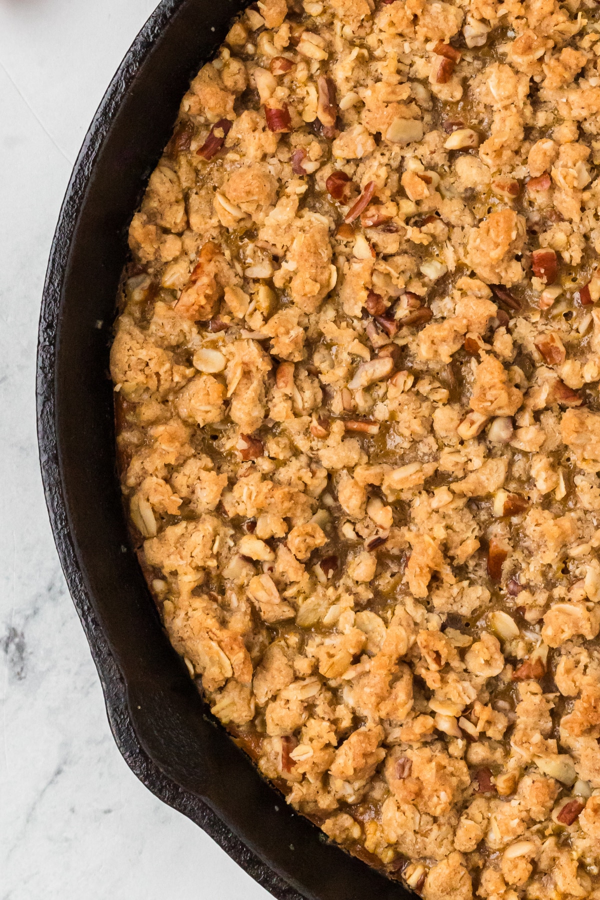 Buttery oat clusters and chopped pecans baked golden over a creamy spiced pumpkin filling. Close-up of golden brown oat and pecan crisp topping baked in a cast-iron skillet.