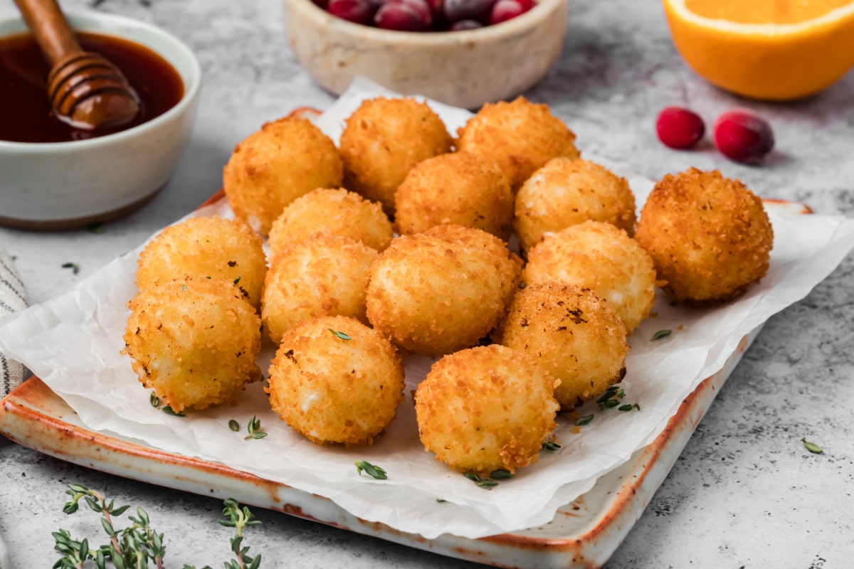 Golden fried goat cheese balls coated in crispy panko breadcrumbs on a serving platter with cranberry hot honey on the side.