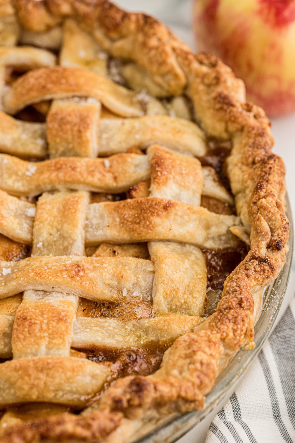 Close-up of golden brown lattice pie crust sprinkled with flaky sea salt, with caramel apple filling visible between the pastry strips.