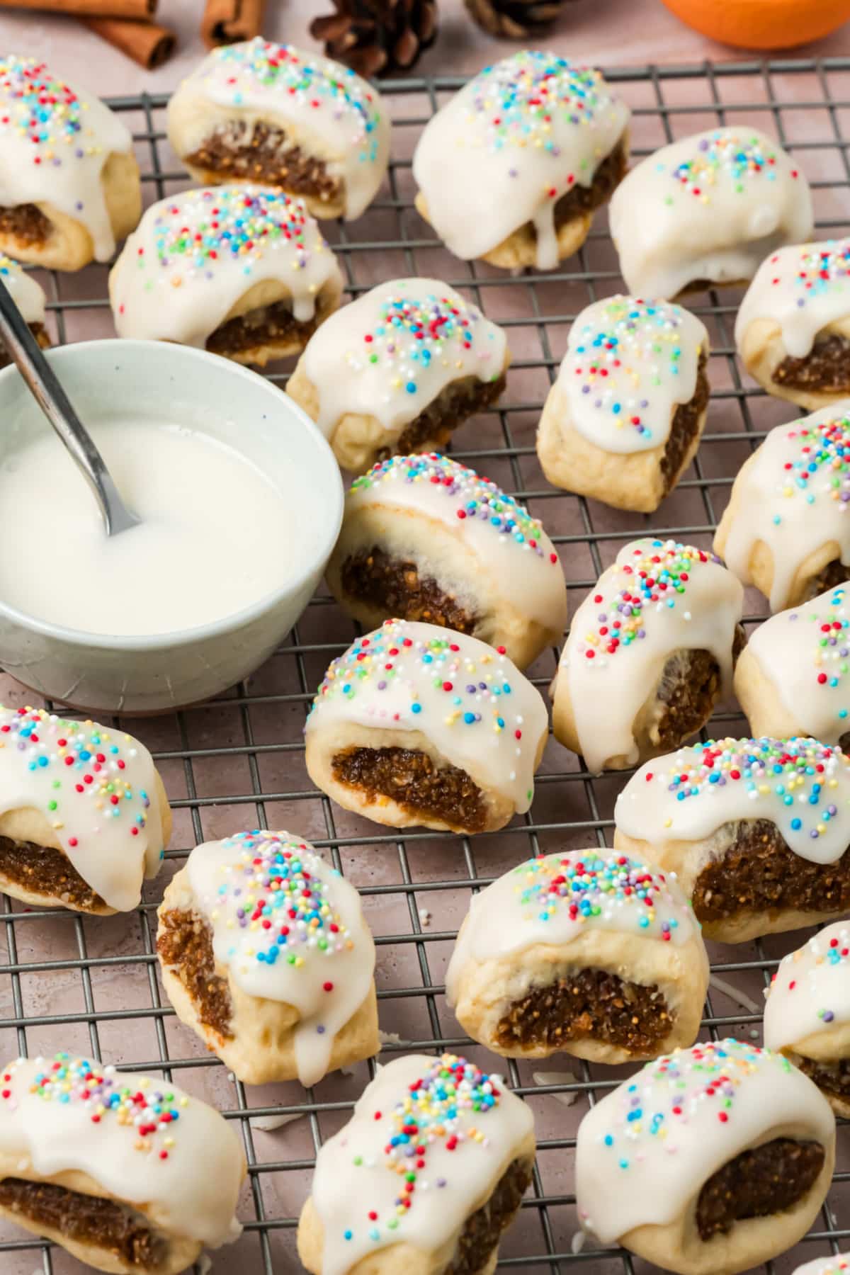 Italian Fig Cookies with Vanilla Glaze and Rainbow Sprinkles Italian fig cookies (cuccidati) filled with dried figs and walnuts, topped with white vanilla glaze and colorful rainbow sprinkles.