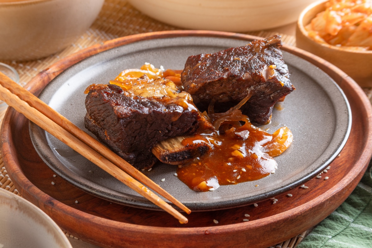Bone-In Korean Braised Short Ribs with Gochujang Sauce Two Korean braised short ribs on a gray plate with softened onions and thickened gochujang sauce.