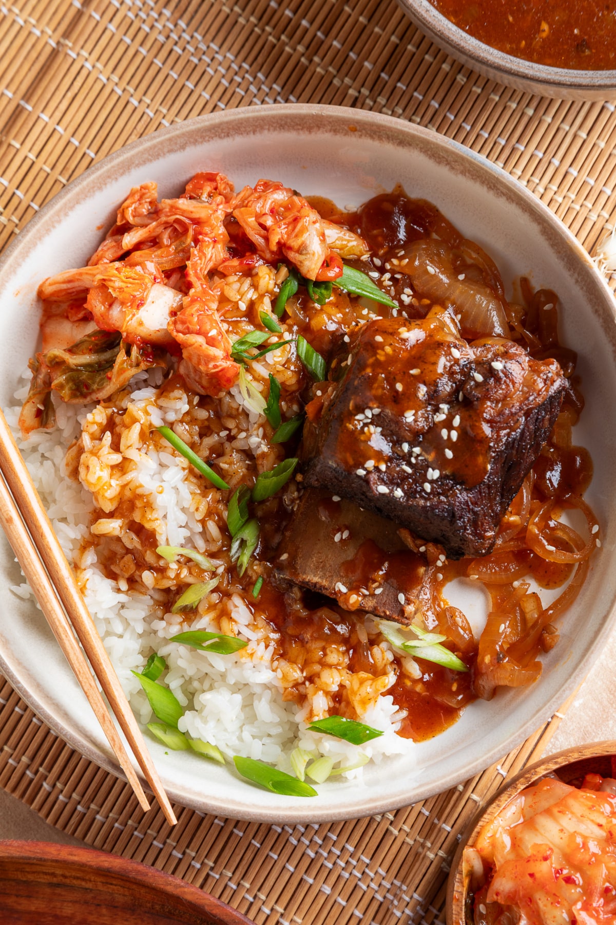 Slow Cooker Korean Braised Short Ribs with Gochujang Sauce Korean braised short ribs served over white rice with gochujang sauce, kimchi, green onions, and sesame seeds.